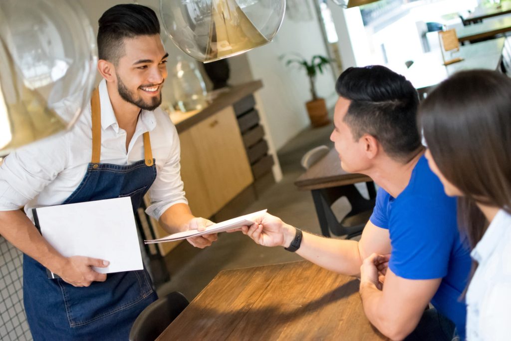 نادل يقدم قائمة الطعام لزبائن في مطعم عربي عصري في مونتريال، يرمز لجودة الخدمة وحفاوة الاستقبال.