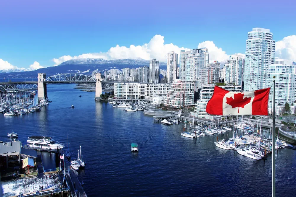 مدينة في كندا يوجد بها ابنية على الساحل ويوجد علم كندا في الصورة بالاضافة لسفن و يخوت