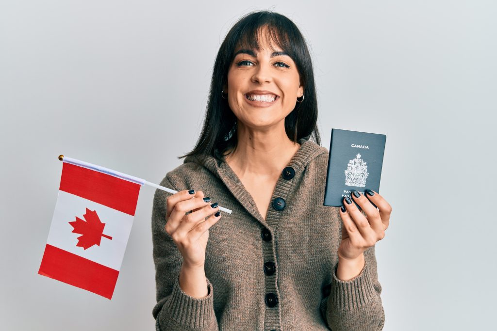 امرأة مبتسمة تحمل بفخر العلم الكندي وجواز السفر الكندي.