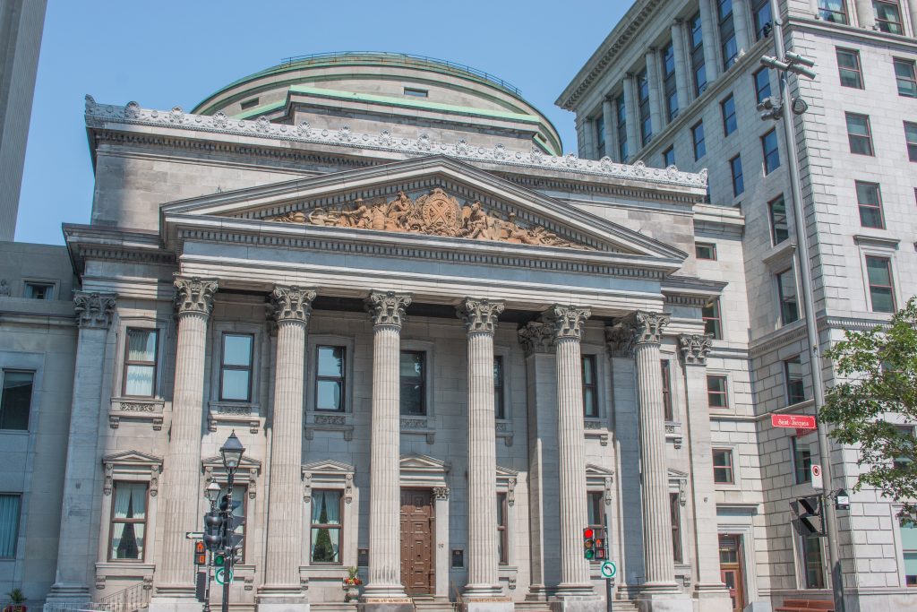 مبنى بنك مونتريال على الطراز الكلاسيكي الجديد مع أعمدة كورنثية وقوس مفصل تحت سماء زرقاء صافية.