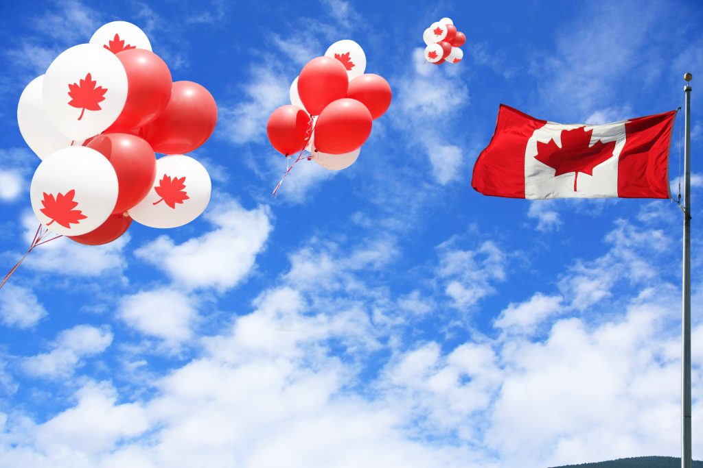 بالونات حمراء بزخارف أوراق القيقب تطفو في السماء بجانب العلم الكندي.