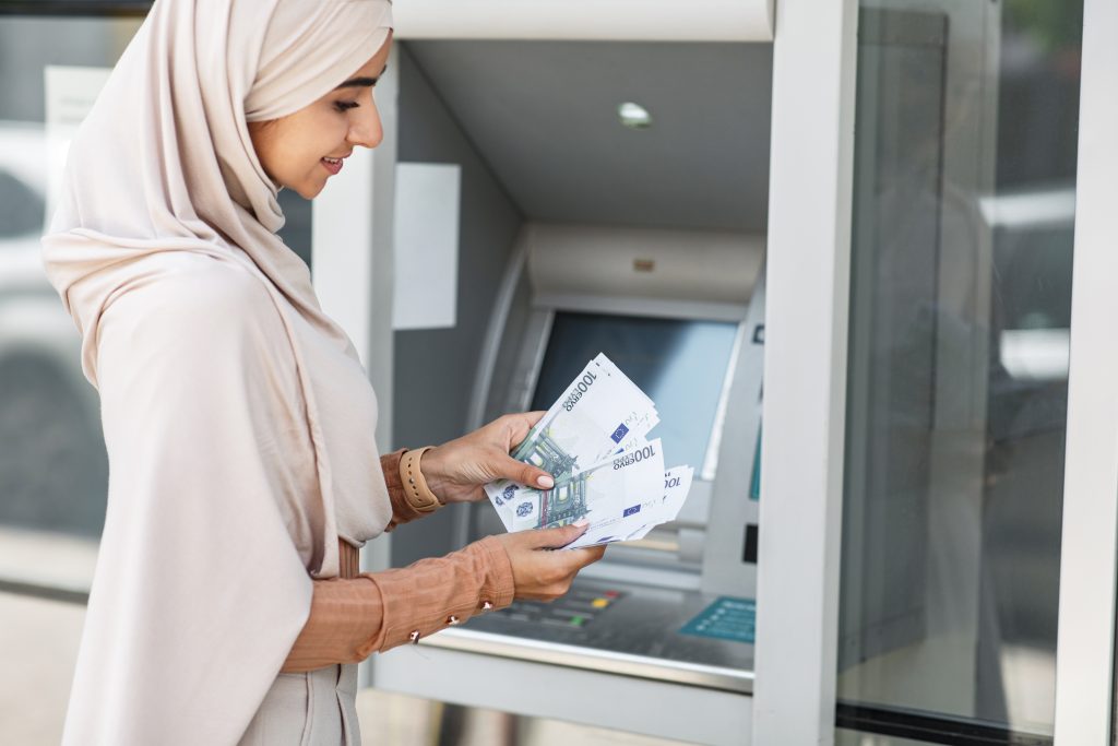 امرأة محجبة تبتسم أثناء سحب الأموال من ماكينة الصراف الآلي لبنك إسلامي في كندا.
