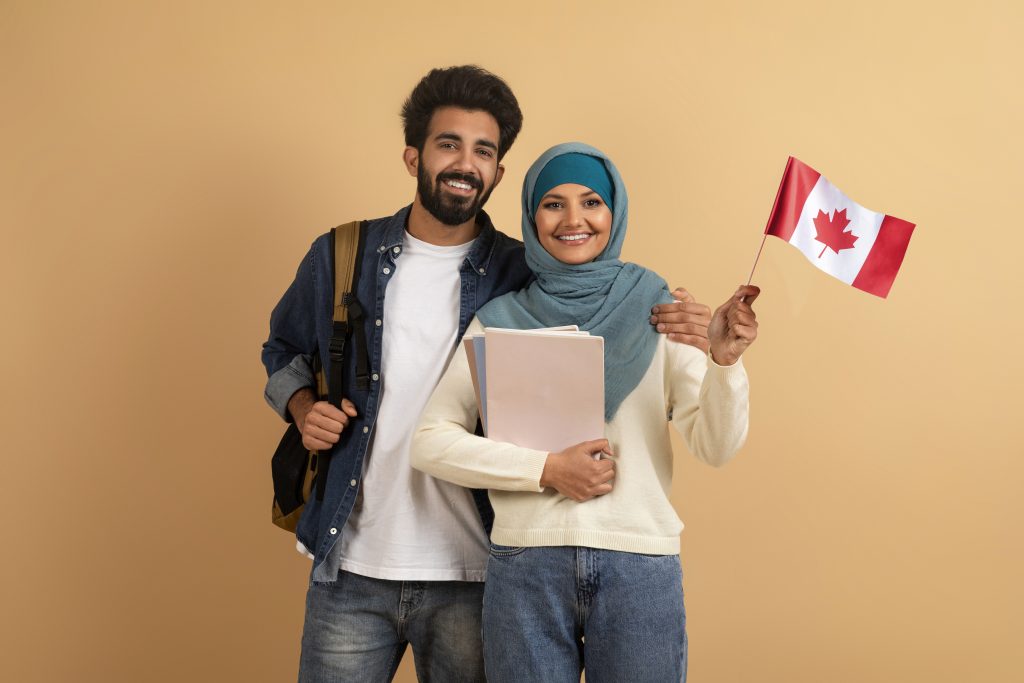 طالبان يبتسمان أحدهما يحمل دفترًا والآخر يلوح بالعلم الكندي ويقفان على خلفية باللون البيج.