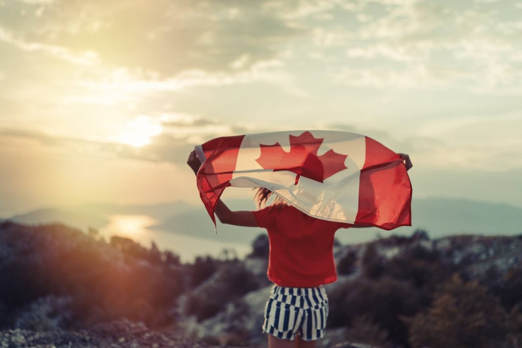 فتاة تقف على تلة وتحمل علمًا كنديًا كبيرًا.