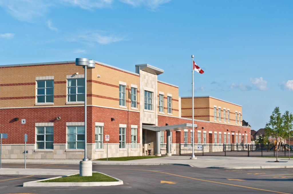 مبنى مدرسة ابتدائية حديث يرفرف العلم الكندي بشكل بارز أمام واجهة من الطوب، تحت سماء زرقاء صافية.