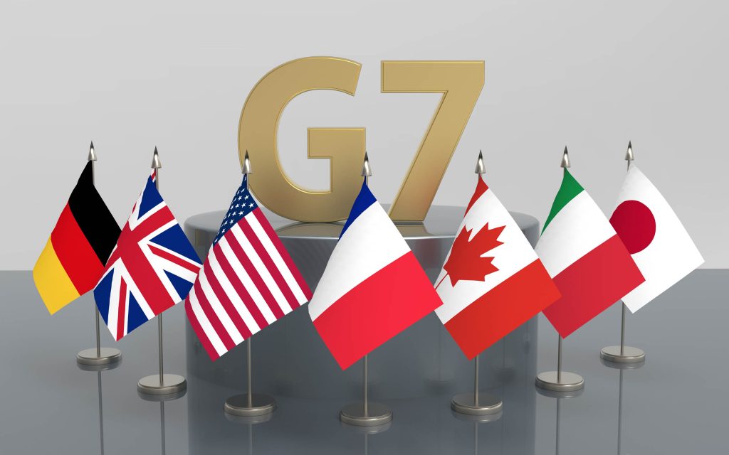 أعلام الدول السبع معروضة أمام علامة g7 الذهبية.