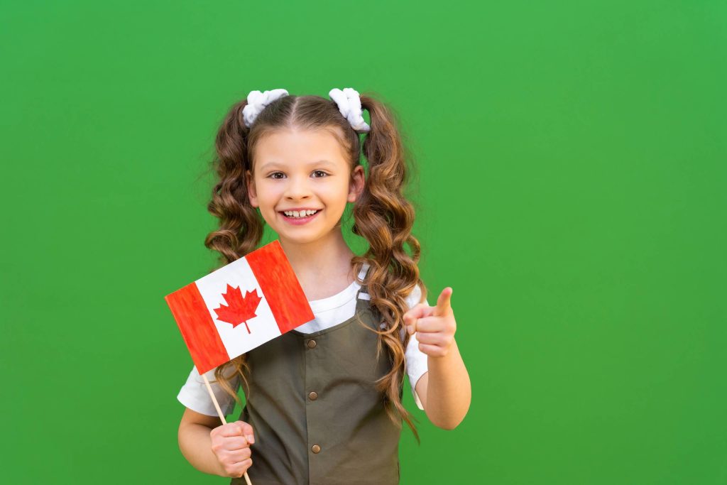 فتاة صغيرة ذات شعر مجعد، تحمل العلم الكندي، ترفع إبهامها لأعلى على خلفية خضراء.