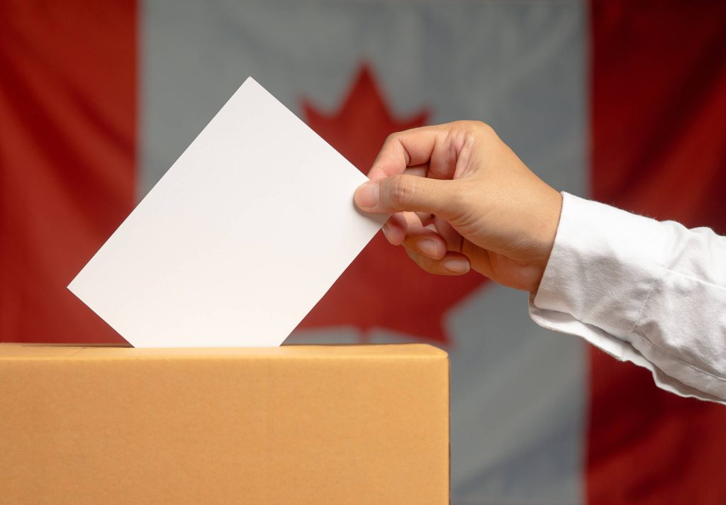 شخص يضع بطاقة اقتراع في صندوق، مع وجود العلم الكندي في الخلفية.