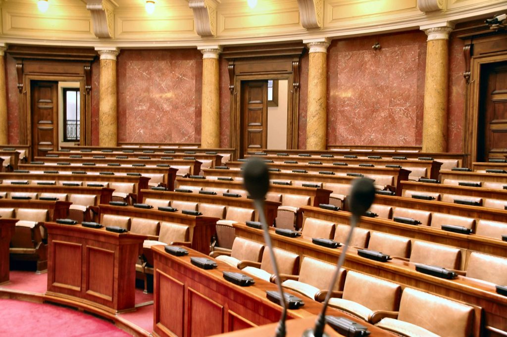 غرفة برلمانية كندية فارغة بها صفوف من المكاتب الخشبية والميكروفونات وسجاد أحمر وجدران رخامية.