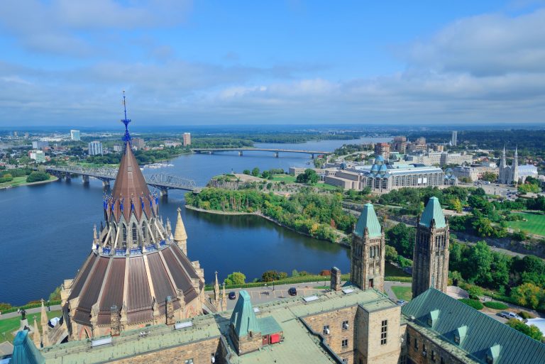 Aerial view of a city by the river with a large building with a pointed roof, bridges, other buildings and green spaces