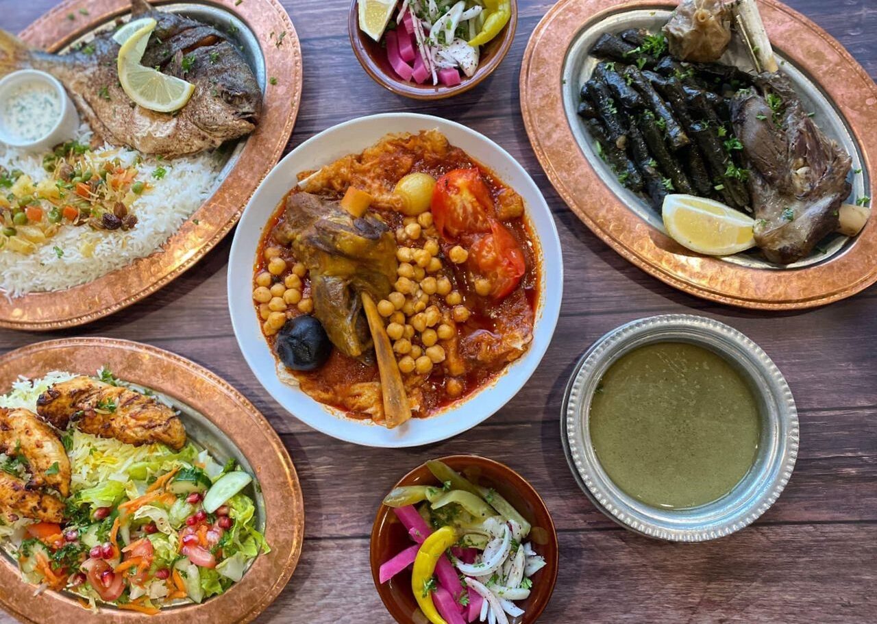 A variety of oriental dishes are arranged on a table, including grilled fish with rice and vegetables, stuffed vine leaves with meat, decorated with lemon slices, and pickles.