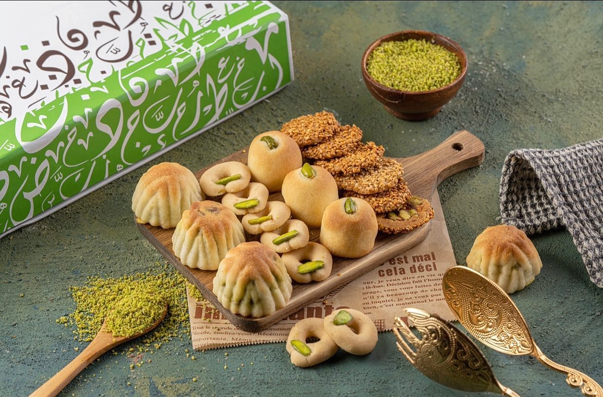 A variety of oriental sweets arranged on a wooden board, including maamoul and barazek.