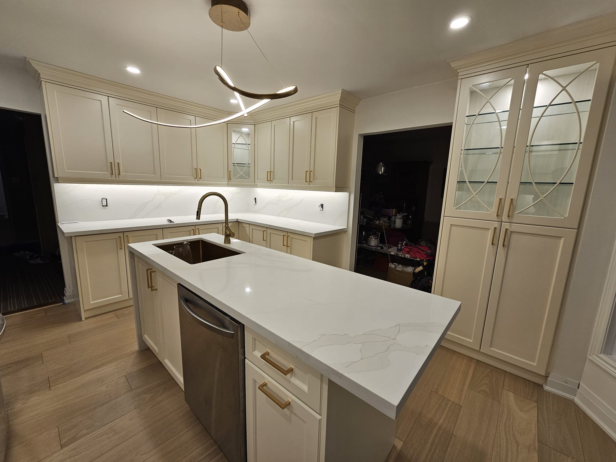 Modern kitchen featuring glossy white cabinets, wooden flooring and elegant lighting.