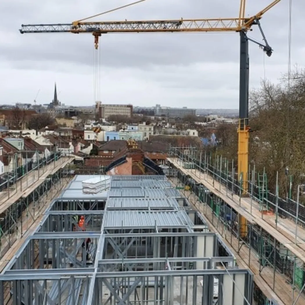 Construction site showing a large crane in the background with a metal structure under construction in the foreground.