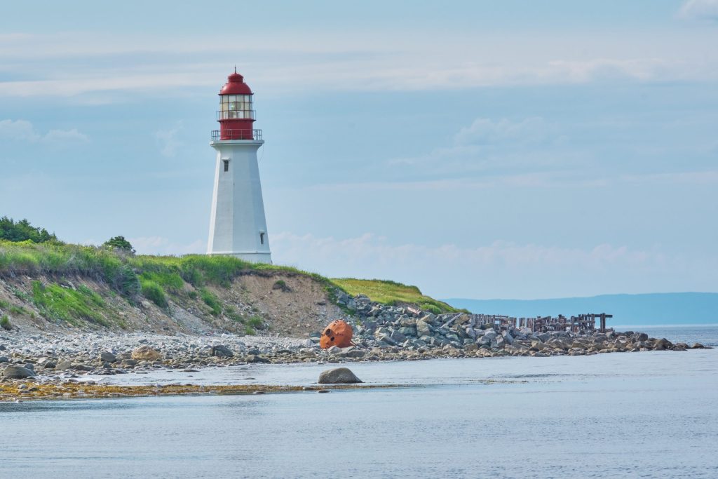 منارة بيضاء ذات قمة حمراء تقف على جرف عشبي على ساحل صخري في نوفا سكوشا